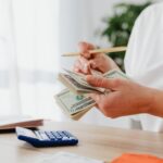 Person using calculator and pen to review monthly bills, key elements in upper frame, landscape finance photo with no text